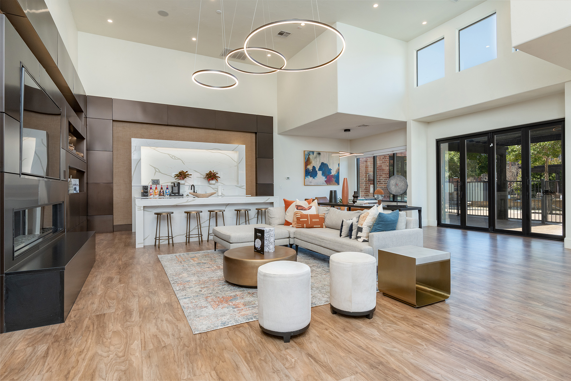 Modern living space featuring a large seating area, bar with stools, contemporary lighting, and floor-to-ceiling windows offering plenty of natural light. This exquisite multi-family real estate investment also includes abstract wall art and a patterned rug for a sophisticated ambiance.