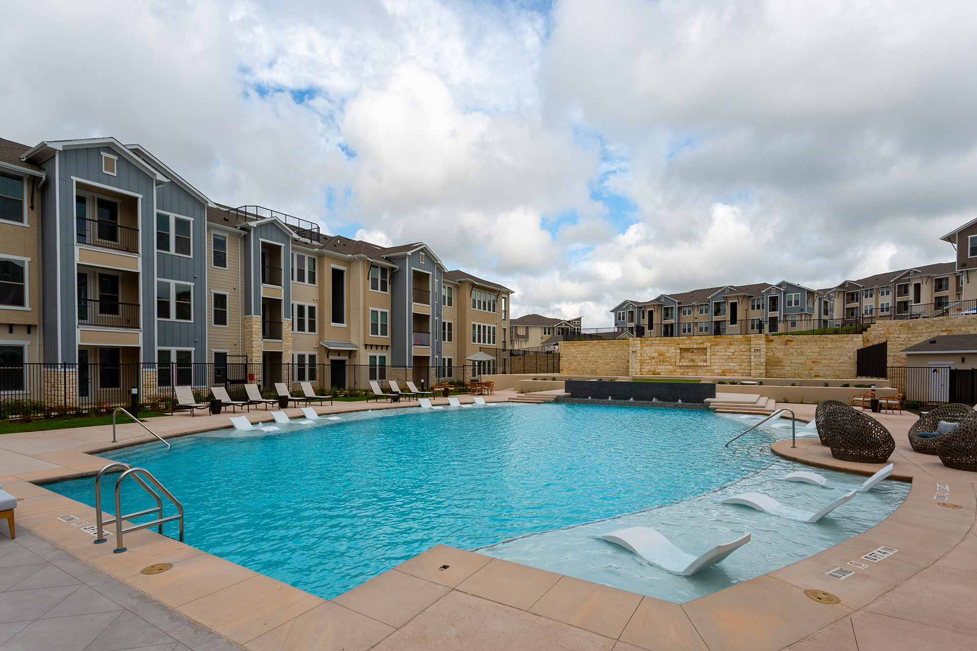An outdoor swimming pool surrounded by lounge chairs and modern apartment buildings under a partly cloudy sky exemplifies prime multi-family real estate investments.
